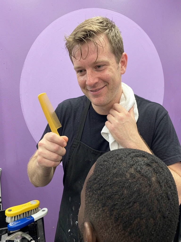 Pessoa cortando o cabelo de um homem com máquina, em ambiente de salão de beleza.